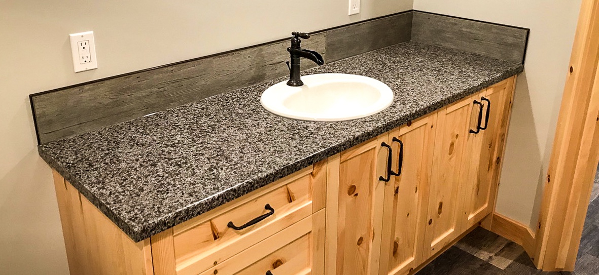 Simple Bathroom renovation project west of Lethbridge. This basement bathroom sink needed to be durable and cost effective, but still look nice. The cabinets have an organic/untreated wood appearance, toped with a dark faux granite, a rustic faucet, and dark wooden trim.