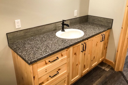 Simple Bathroom renovation project west of Lethbridge. This basement bathroom sink needed to be durable and cost effective, but still look nice. The cabinets have an organic/untreated wood appearance, toped with a dark faux granite, a rustic faucet, and dark wooden trim.